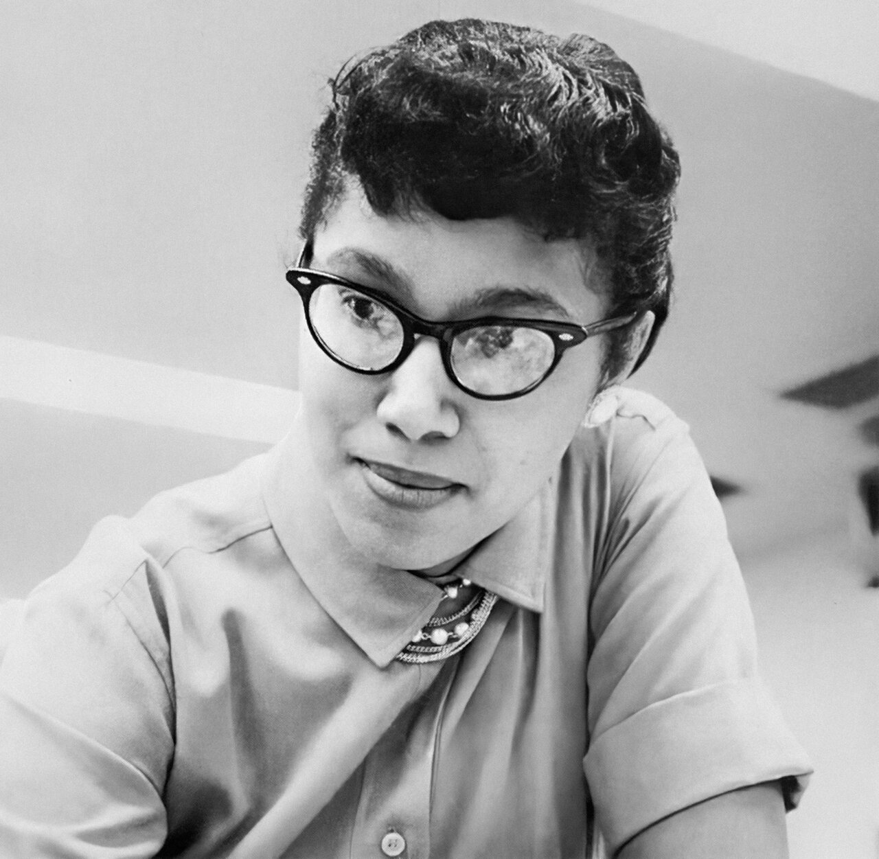 Black and white portrait of a woman wearing cat-eye glasses and a collared shirt with decorative brooch.