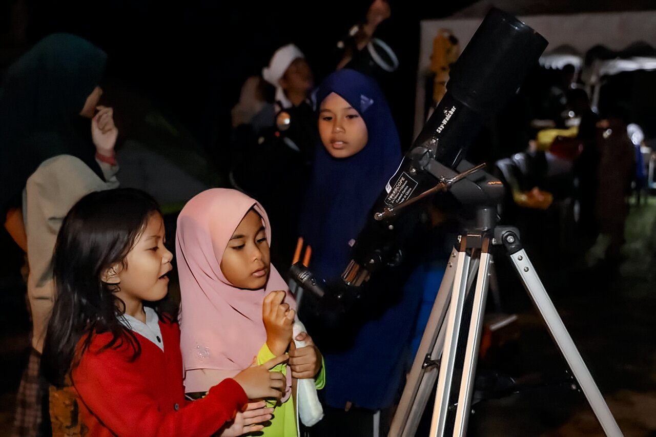 Children and adults look through a telescope at night during an astronomy outreach event.